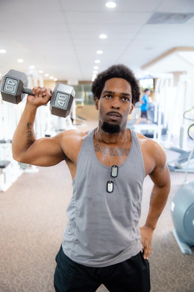 man in gray tank top holding black dumbbell
